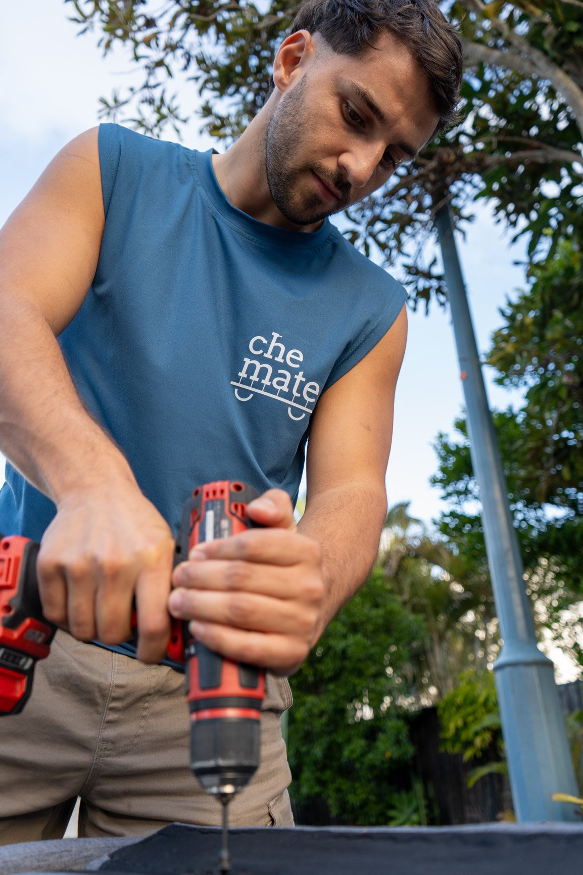 Che Mate worker using a drill on an outdoor build, tools in hand